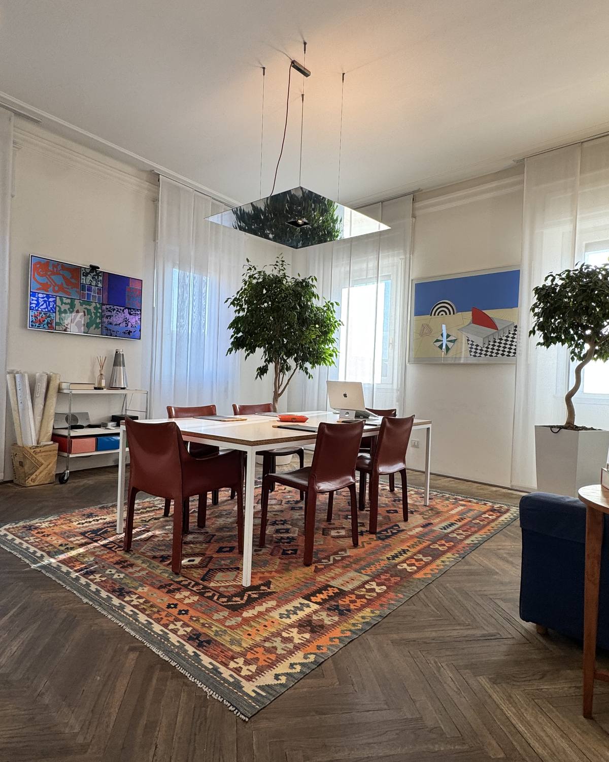 L’ufficio de L’Ambrosiana Immobiliare in Via Santa Lucia: il tavolo delle riunioni con le sedie in cuoio, il tappeto kilim sul parquet a spina di pesce, piante e quadri alle pareti.